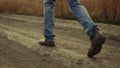 Man farmer legs in shoes passing farmland rural road. Rubber boots close up.