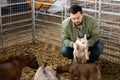 Farmer squatting with goatling in shed