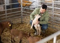 Farmer squatting with goatling in shed