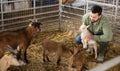 Farmer squatting with goatling in shed