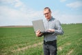 Man farmer working on a laptop in the field. Agronomist examines the green sprout winter wheat Royalty Free Stock Photo