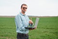 Man farmer working on a laptop in the field. Agronomist examines the green sprout winter wheat Royalty Free Stock Photo