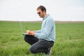 Man farmer working on a laptop in the field. Agronomist examines the green sprout winter wheat Royalty Free Stock Photo