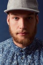 Man, fashion and face with hat in a studio, denim and trendy isolated on blue background. Irish model with hipster beard