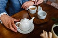 Man in a fashionable suit pours tea from a teapot in a mug. Rules of etiquette in a cafe. Man takes care of a woman. A young coupl Royalty Free Stock Photo