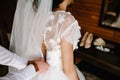 The man fastens buttons on the corset on the dress. Bride in white wedding dress with lace standing in the room Royalty Free Stock Photo