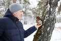 Man feeds squirrel while standing by tree in snowy forest during winter Royalty Free Stock Photo