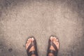 Man feet wearing some brown flip flops standing on the asphalt concrete floor