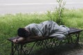 The man fell asleep, lying on the wooden seat, covered his face with a cap