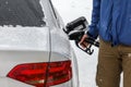 Man filling fuel to his diesel car at gas station in winter. Detail on snow covered tank cover and pump nozzle Royalty Free Stock Photo