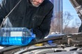 Man filling a windshield washer tank of a car by antifreeze on winter Moscow street Royalty Free Stock Photo