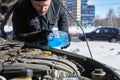 Man filling a windshield washer tank of a car by antifreeze on winter Moscow street Royalty Free Stock Photo