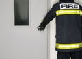 A man in a fireman`s uniform opens the door, rear view