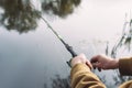 Man fisherman catches a fish on a fishing rod with a reel on the lake against the background of the forest and sky with clouds Royalty Free Stock Photo