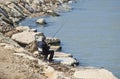 Man fishermen sitting on a small folding chair on stone coast and fish with fishing rod in the sea bay Royalty Free Stock Photo