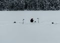 Man fishing from the ice of a frozen lake covered in deep snow