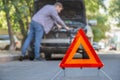 Man fixing car on road. Car Breakdown while driving. Driver looks on breakdown under the hood of car. Red triangular stop sign on Royalty Free Stock Photo