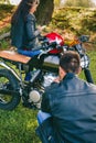 Man fixing his motorcycle while his girlfriend looks at mobile