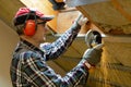 Man fixing metal frame using angle grinder on attic ceiling covered with rock wool