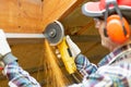 Man fixing metal frame using angle grinder on attic ceiling covered with rock wool