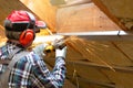 Man fixing metal frame using angle grinder on attic ceiling covered with rock wool