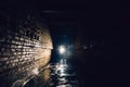 Man with flashlight in dark dirty brick underground tunnel or sewerage corridor