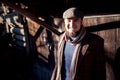 Man in flat cap with old-fashioned outfit outdoors on background of wooden constructions.