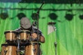 Man With Flat Cap Playing Wooden Caribbean Bongo Drums With Mircophone And Chimes And Green Curtain Behind