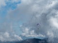 A man flies a paraglider over the mountains against a blue sky and cloud haze