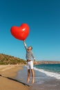 A man flying with big heart balloon on tropical beach. Summer love concept