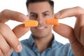 Man with foam ear plugs against white background, focus on hands