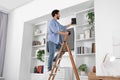 Man on wooden folding ladder taking books from shelf at home Royalty Free Stock Photo