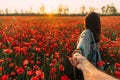 Man follows a woman in poppy meadow at sunset.