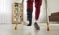 Man with foot or leg injury wearing support brace and walking with crutches in living room