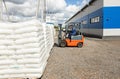 A man on a forklift works in a large warehouse, unloads bags of raw materials into a truck for transportation