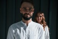 Man is in front of woman. Beautiful young couple is standing together against dark green background Royalty Free Stock Photo