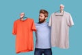 Man frowning face holding two hangers with gray and orange T-shirts, hard to choose the best attire. Royalty Free Stock Photo