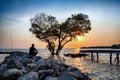 man in frustrated depression sitting alone on the rock dam extended into the sea and looking at tree in the shape of heart on sun Royalty Free Stock Photo