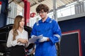 Man garage worker and woman customer talking to discuss the details of car repairs. male mechanic holding clipboard and writes Royalty Free Stock Photo