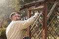 The man in the garden paints brown wooden boards of the garden furniture. Renovation and maintenance of garden pergolas. Royalty Free Stock Photo