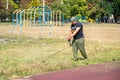 Man gardener mowing grass with electric or petrol lawn trimmer around the sports ground. Worker mows grass with a gasoline scythe Royalty Free Stock Photo