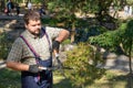 Man gardener in protective gloves with garden shears, scissors or secateurs cutting a thuja or juniper topiary hedge in public Royalty Free Stock Photo