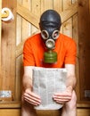 Man in gas-mask sitting in toilet with newspaper