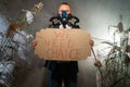 A man in a gas mask in a suit shrouded in smoke is walking in a dangerous radioactive zone with a poster We Need Change