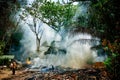 A man in a gauze bandage and a fire hose trying to put out the fire in the forest. Fire and smoke in the jungle.  Fills with water Royalty Free Stock Photo