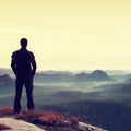 Man gesture triumph. Satisfy hiker in dark sportswear at edge with heather.Tall man on the peak of sandstone cliff watching to lan Royalty Free Stock Photo