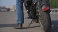 A man gets on an electric motorcycle, removes the kickstand and rides off.