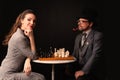 A man with a girl plays chess and smokes a pipe on a dark background