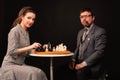 A man with a girl plays chess and smokes a pipe on a dark background