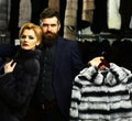 Man and girl with serious faces hold furry coats